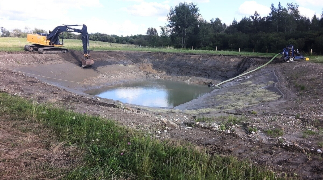 Excavator and pump beside a partially drained pond